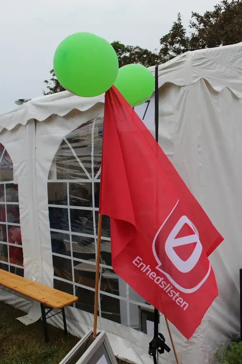 Red Enhedslisten flag with green balloons beside a white tent
